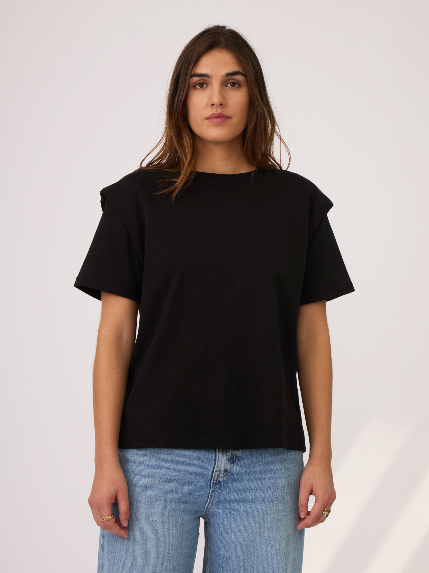 Camiseta negra con detalle en los hombros. simulando unas hombreras que se ajustan bien a la figura. Es un largo ideal para usar por dentro o por fuera y va a ser una pieza indispensable en el closet ya que se puede combinar con diferentes outfits.