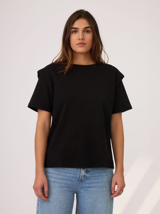 Camiseta negra con detalle en los hombros. simulando unas hombreras que se ajustan bien a la figura. Es un largo ideal para usar por dentro o por fuera y va a ser una pieza indispensable en el closet ya que se puede combinar con diferentes outfits.