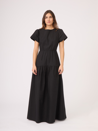 El Vestido Lison es un vestido largo de mangas cortas, con un corte de falda en A que comienza desde la cintura y un escote discreto en la parte baja de la espalda. El color negro es ideal para que pueda usarse en ocasiones casuales o elegantes.